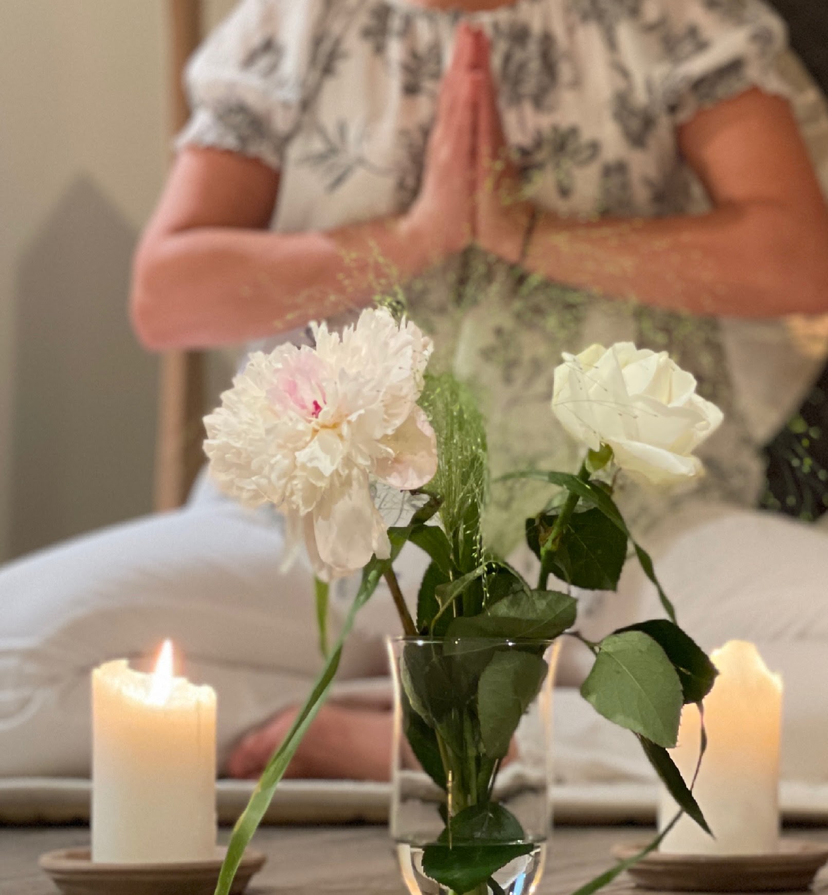 Två tända ljus och blommor framför en yogande kvinna